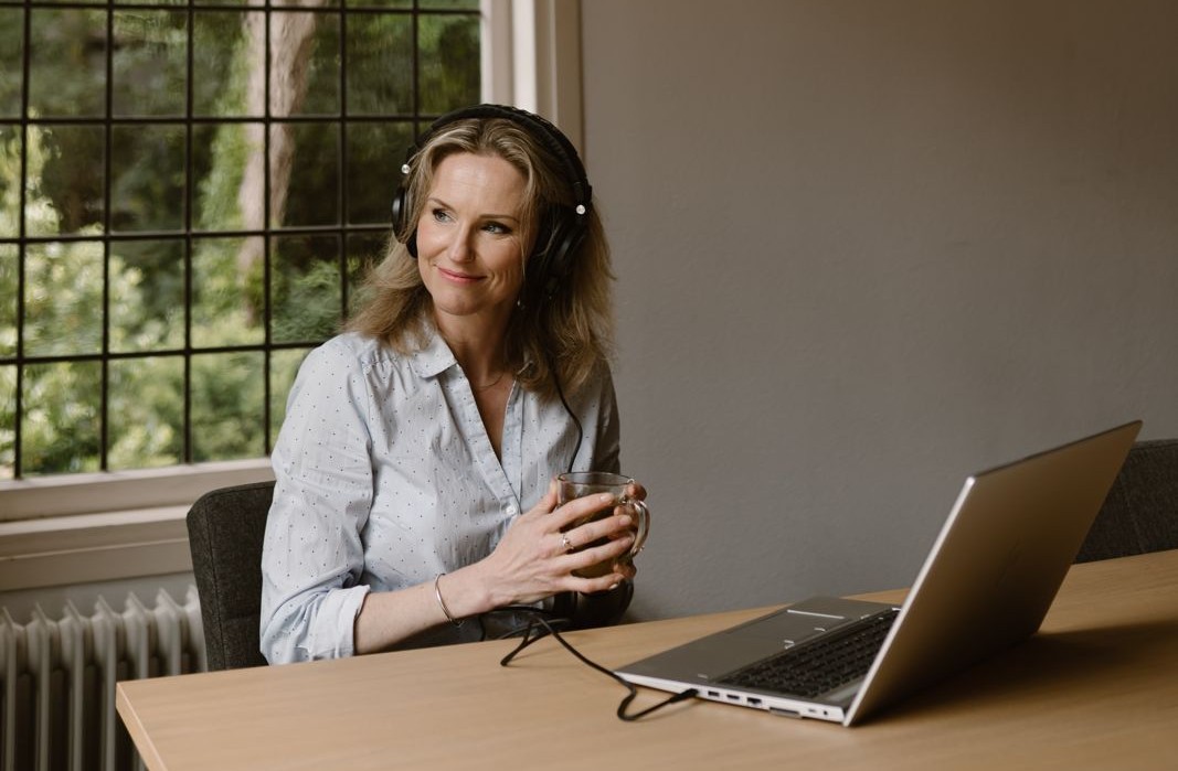 Vrouw met koptelefoon luistert naar de Synco-audioreeks bij een raam met uitzicht op groen.